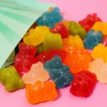 Close-up of colorful gummy bears spilling out of a high-strength package on a pink surface.