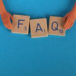 Flat lay of scrabble tiles spelling 'FAQ' with toy hands on a blue background, creating a conceptual image.