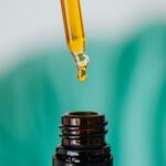 Closeup of anonymous doctor with pipette for fluid dripping yellow medication in brown glass vial while making procedure in clinic