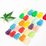 Vibrant assorted gummy bears arranged with a cannabis leaf on a white background.