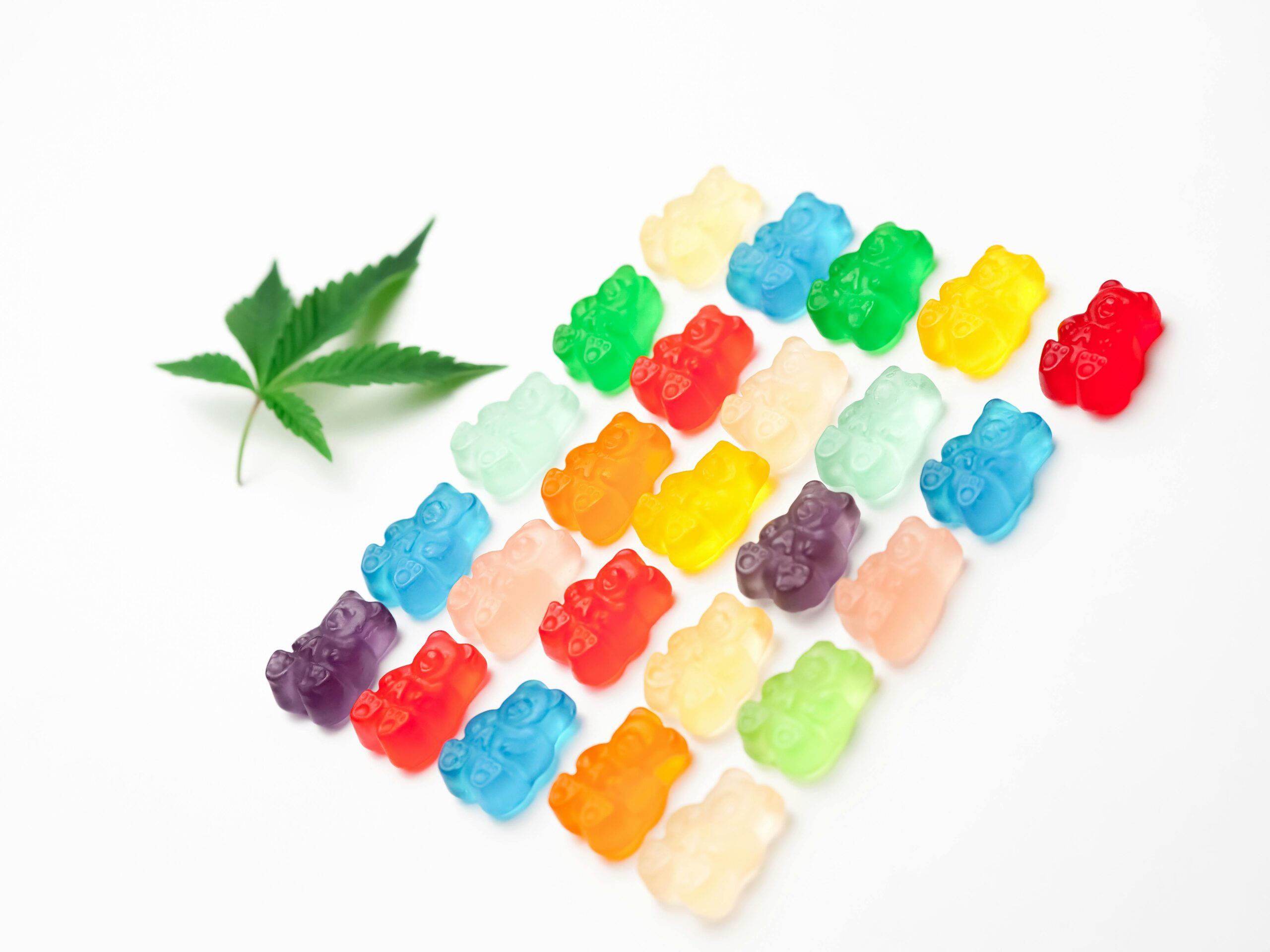 Vibrant assorted gummy bears arranged with a cannabis leaf on a white background.